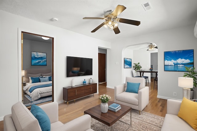 living area with ceiling fan, arched walkways, light wood-style flooring, baseboards, and visible vents