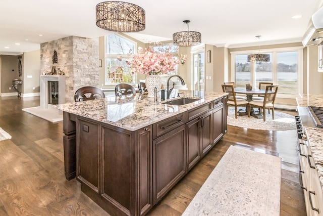 kitchen with an inviting chandelier, light stone counters, baseboard heating, dark brown cabinets, and a sink