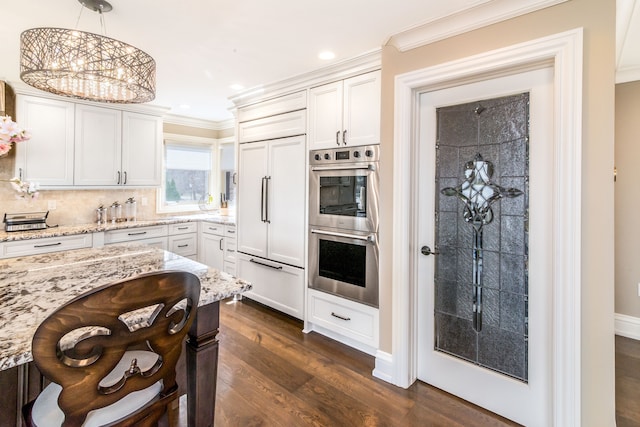 kitchen featuring light stone countertops, stainless steel double oven, paneled refrigerator, crown molding, and dark wood-type flooring