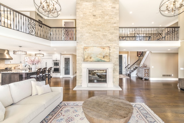 living room featuring a large fireplace, a chandelier, visible vents, stairs, and a high ceiling