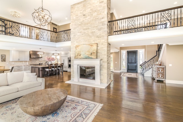 living area featuring dark wood finished floors, stairs, a chandelier, ornamental molding, and a towering ceiling