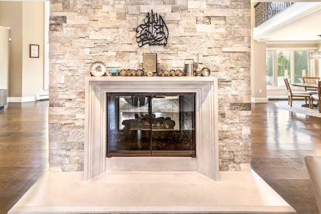 details featuring a stone fireplace, baseboard heating, wood finished floors, and baseboards