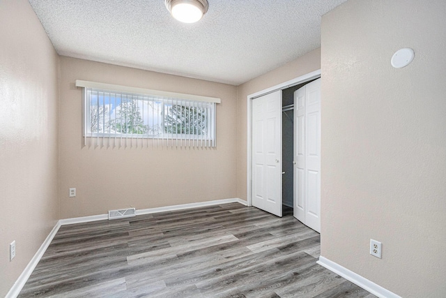 unfurnished bedroom with visible vents, a closet, baseboards, and wood finished floors