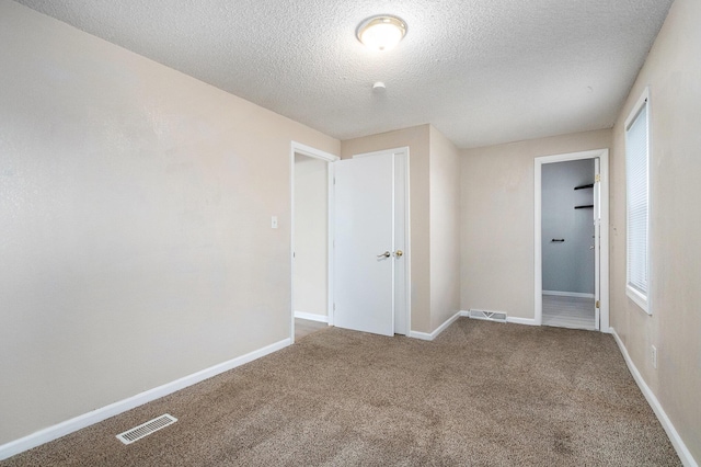 unfurnished bedroom with a textured ceiling, baseboards, visible vents, and carpet floors