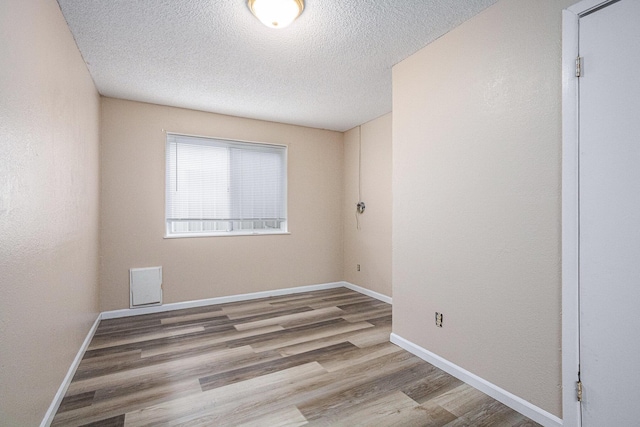 spare room featuring a textured ceiling, wood finished floors, baseboards, and visible vents