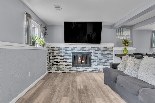 living area with a brick fireplace, visible vents, and wood finished floors