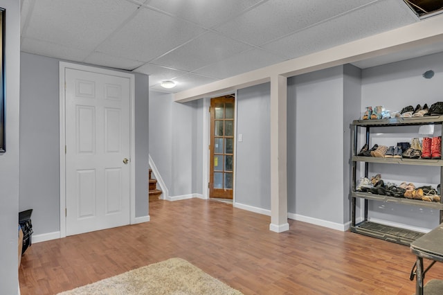finished below grade area with stairway, wood finished floors, a drop ceiling, and baseboards