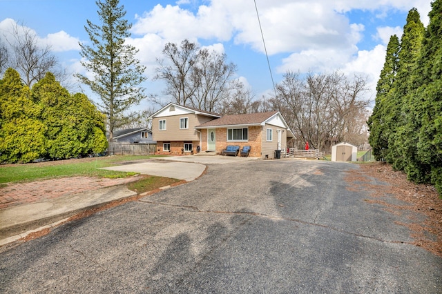 split level home featuring brick siding, an outdoor structure, a shed, aphalt driveway, and fence