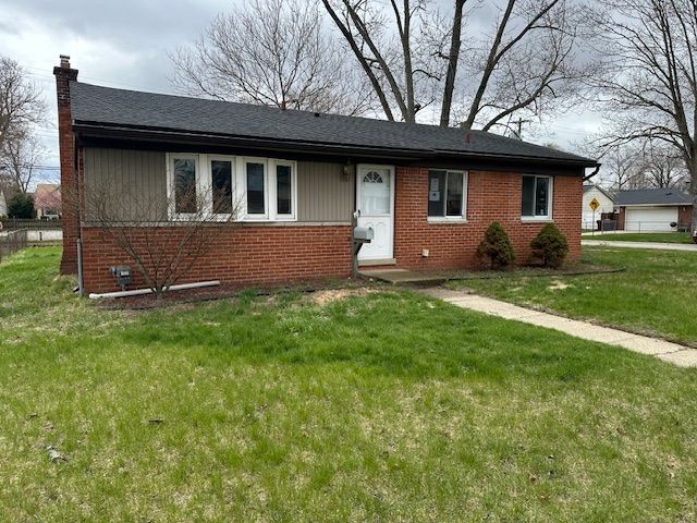 view of front of house with brick siding, a chimney, and a front lawn