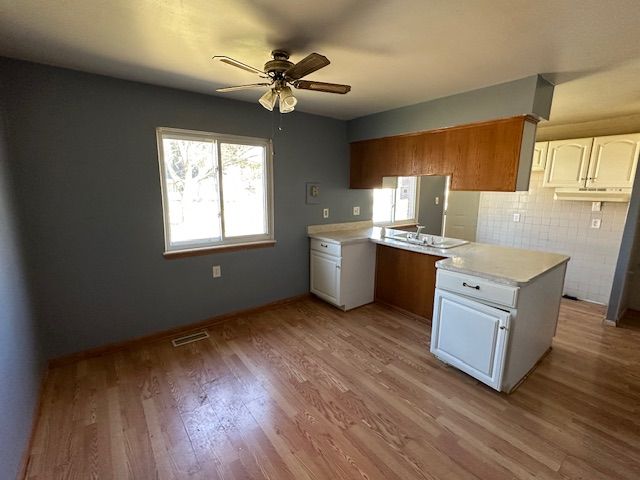 kitchen with a peninsula, visible vents, light wood finished floors, light countertops, and a ceiling fan
