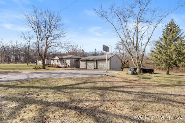 view of home's exterior with a yard, driveway, a garage, and an outbuilding