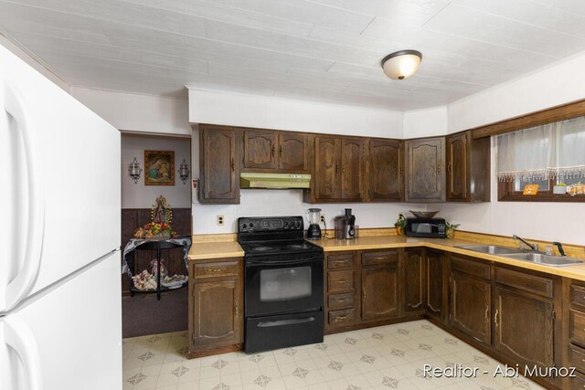kitchen with light countertops, freestanding refrigerator, under cabinet range hood, black range with electric stovetop, and a sink