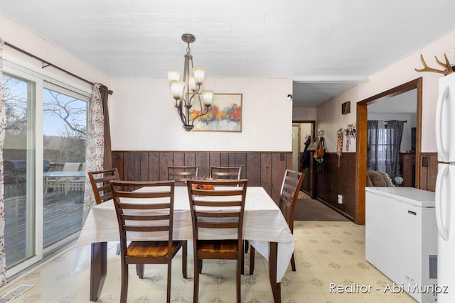 dining space with wood walls, visible vents, an inviting chandelier, and a wainscoted wall