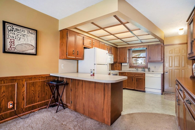 kitchen with white appliances, a peninsula, light countertops, a sink, and brown cabinets