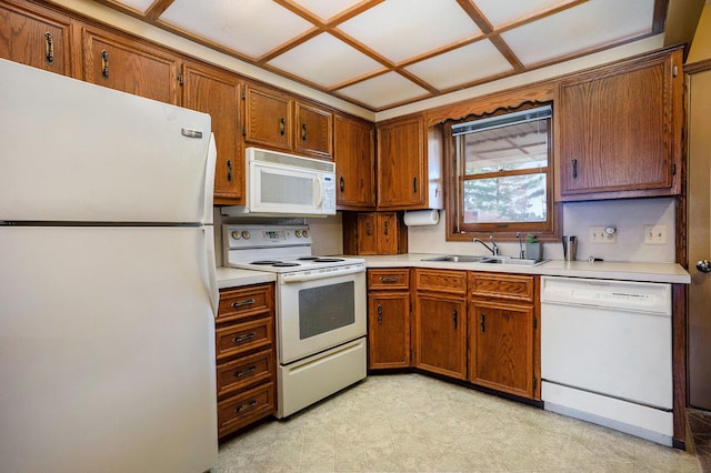 kitchen with a sink, light countertops, white appliances, and brown cabinets