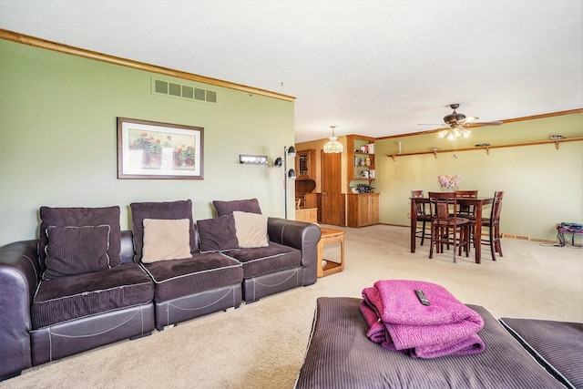 carpeted living area with visible vents, baseboards, crown molding, and a ceiling fan