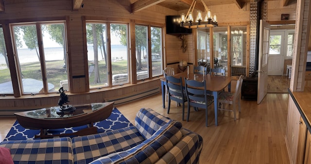 dining space with a baseboard heating unit, an inviting chandelier, wooden walls, light wood-style floors, and beam ceiling
