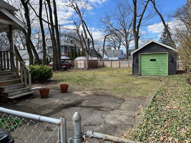 view of yard featuring a shed, a detached garage, an outdoor structure, fence, and driveway