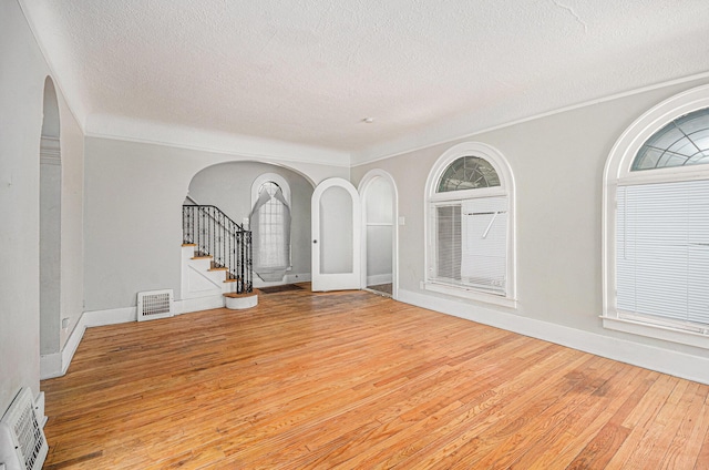 13605 Griggs St, Detroit, MI 48238 - unfurnished living room featuring arched walkways, light wood-type flooring, a textured ceiling, visible vents, and stairway