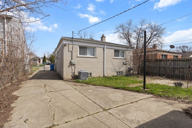 back of property featuring a chimney, driveway, brick siding, central AC, and fence