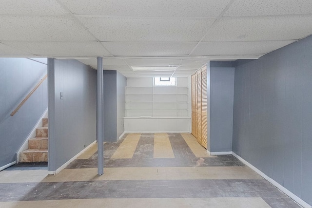 below grade area featuring baseboards, a paneled ceiling, and stairs