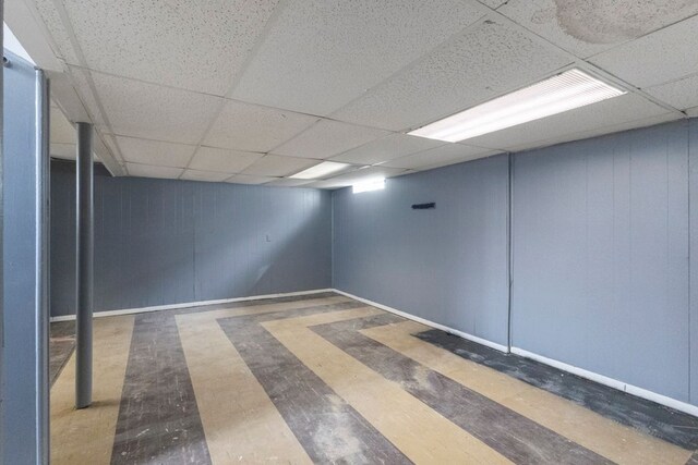 finished below grade area featuring a drop ceiling, baseboards, and wood finished floors