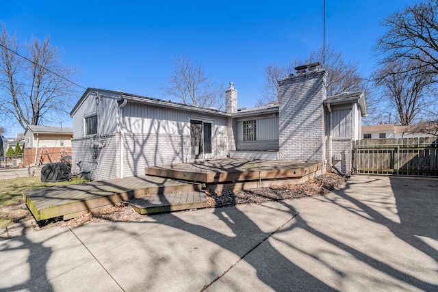 rear view of property with a patio, a chimney, brick siding, a deck, and fence