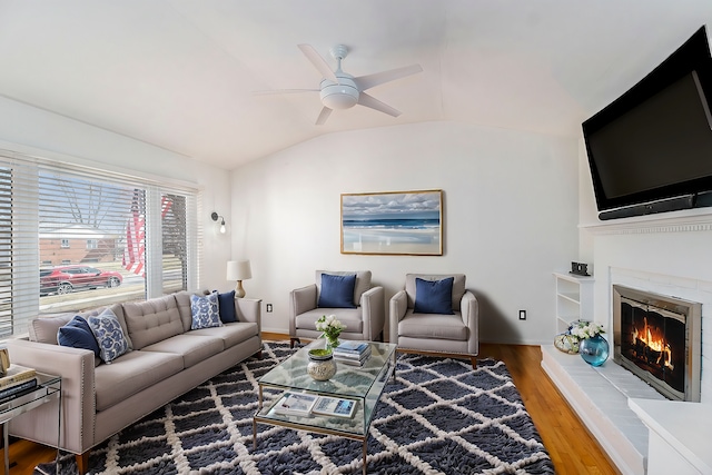 living area featuring baseboards, ceiling fan, wood finished floors, vaulted ceiling, and a glass covered fireplace