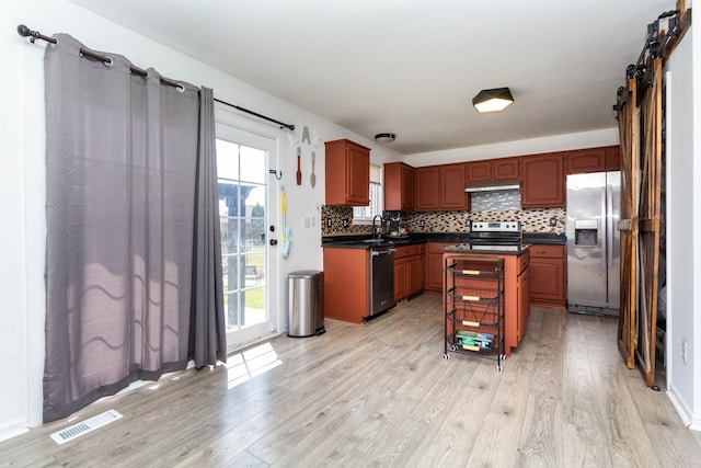 kitchen featuring stainless steel appliances, light wood-style floors, dark countertops, a sink, and tasteful backsplash