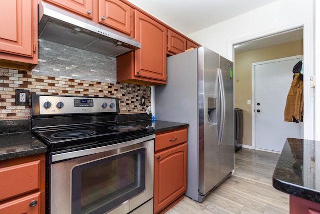 kitchen featuring stainless steel appliances, under cabinet range hood, tasteful backsplash, dark stone counters, and light wood-style flooring