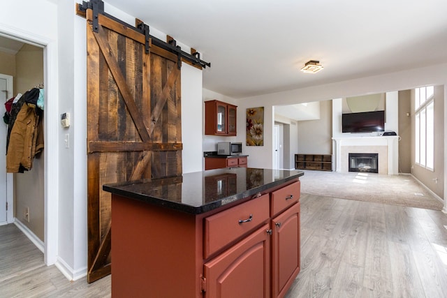 kitchen with stainless steel microwave, light wood-style flooring, a barn door, a glass covered fireplace, and baseboards