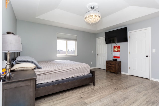 bedroom featuring a tray ceiling, light wood-type flooring, a chandelier, and baseboards