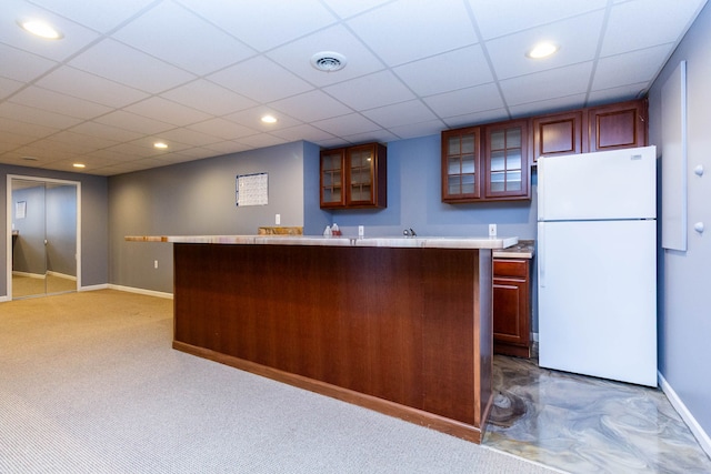 kitchen with freestanding refrigerator, light countertops, baseboards, glass insert cabinets, and a drop ceiling