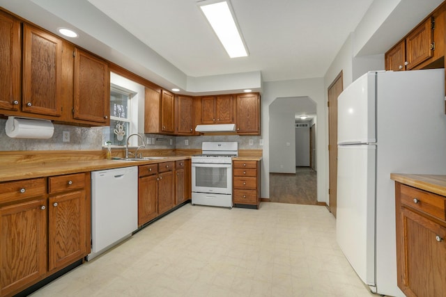 kitchen with white appliances, light floors, under cabinet range hood, a sink, and brown cabinets