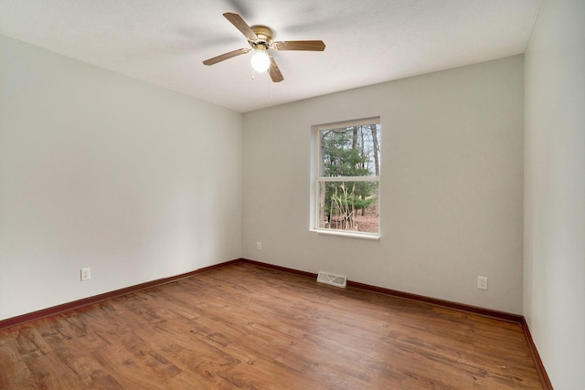 empty room with visible vents, baseboards, a ceiling fan, and wood finished floors