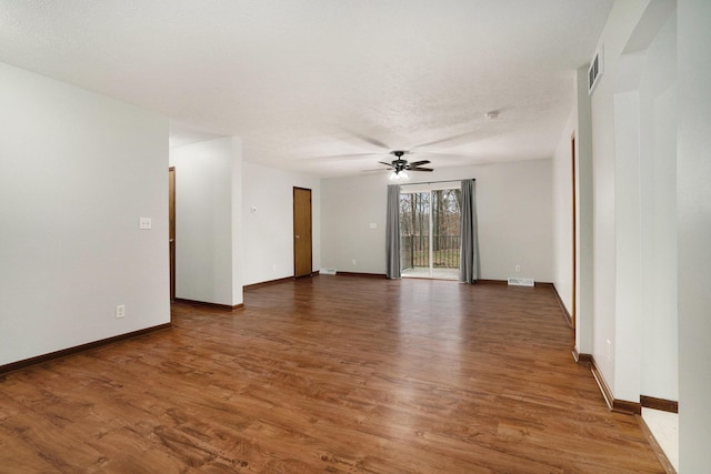 empty room with wood finished floors, baseboards, a ceiling fan, and visible vents