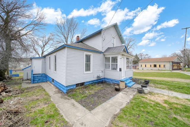 view of side of home featuring a sunroom, a lawn, entry steps, roof with shingles, and a chimney