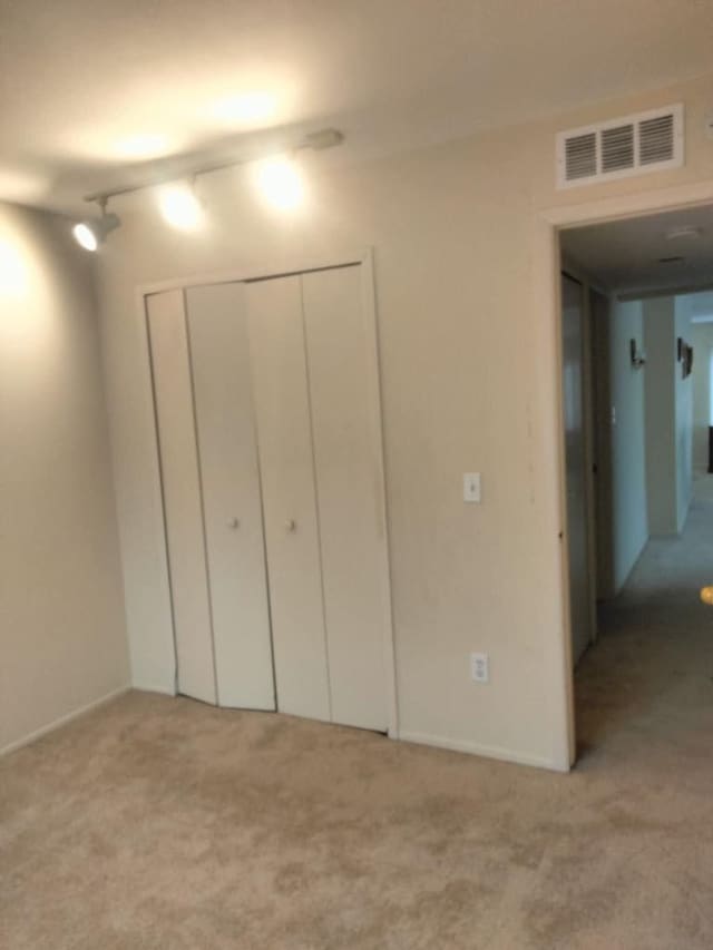 unfurnished bedroom with track lighting, a closet, carpet flooring, and visible vents