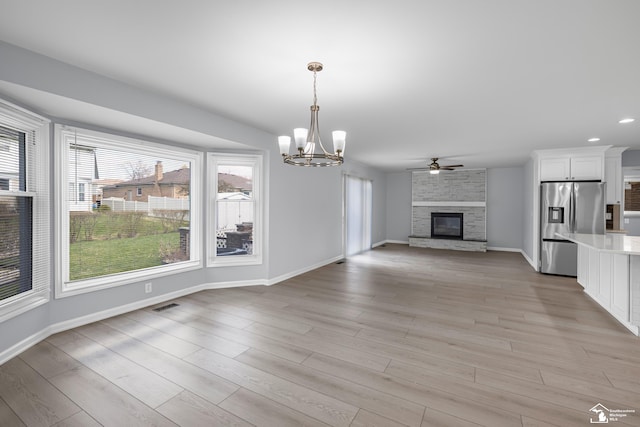 unfurnished dining area with a fireplace, light wood finished floors, ceiling fan with notable chandelier, and baseboards