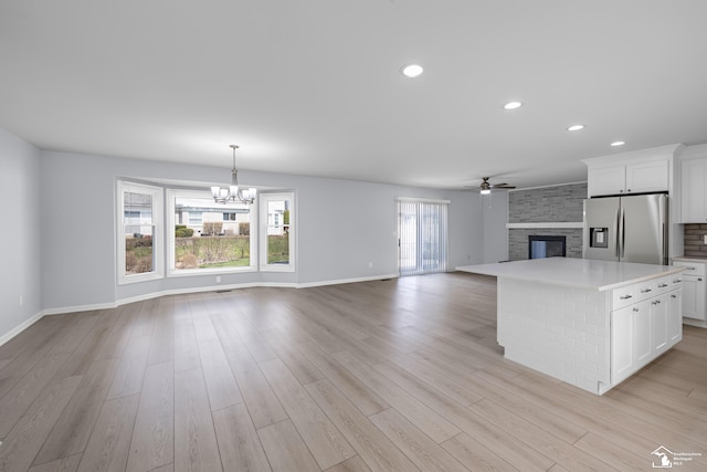 kitchen with ceiling fan with notable chandelier, a fireplace, light countertops, stainless steel fridge, and open floor plan
