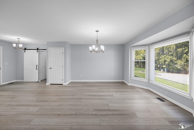 unfurnished dining area featuring a chandelier, a barn door, light wood-style flooring, and baseboards