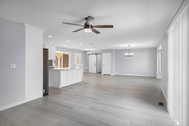 unfurnished living room with visible vents, baseboards, a barn door, light wood-type flooring, and ceiling fan with notable chandelier