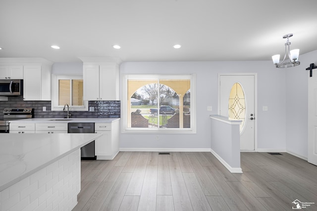 kitchen with white cabinets, a sink, appliances with stainless steel finishes, a chandelier, and light wood-style floors
