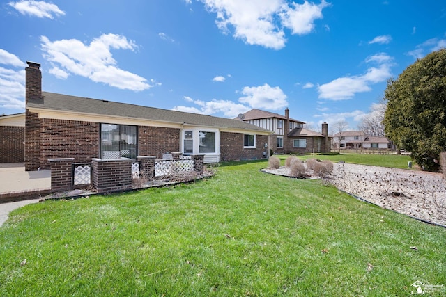 back of house with brick siding, a chimney, and a lawn