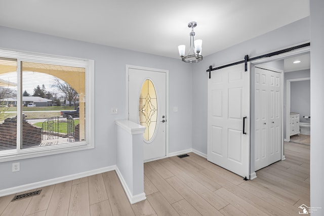foyer featuring a notable chandelier, baseboards, a barn door, visible vents, and light wood finished floors