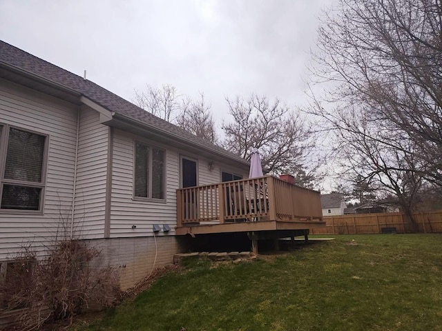 exterior space with a yard, a deck, fence, and a shingled roof