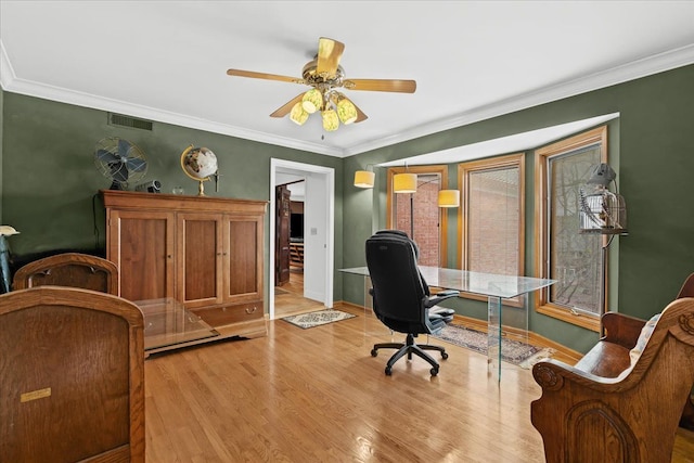 office area with light wood-type flooring, baseboards, visible vents, ceiling fan, and ornamental molding