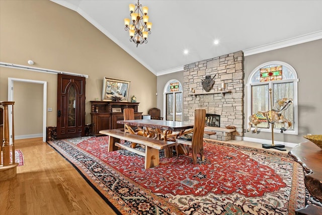 dining area featuring high vaulted ceiling, a stone fireplace, a chandelier, light wood-type flooring, and ornamental molding