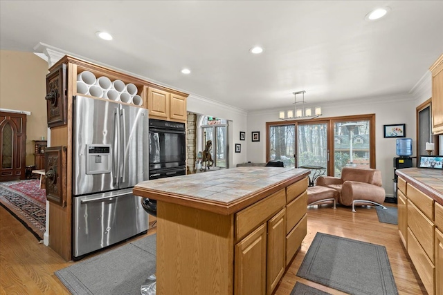 kitchen featuring light wood finished floors, tile countertops, ornamental molding, a center island, and stainless steel fridge