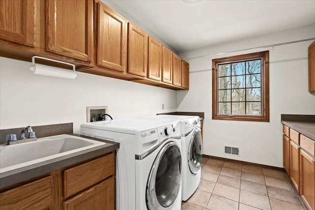 washroom with a sink, light tile patterned floors, washer and dryer, cabinet space, and visible vents